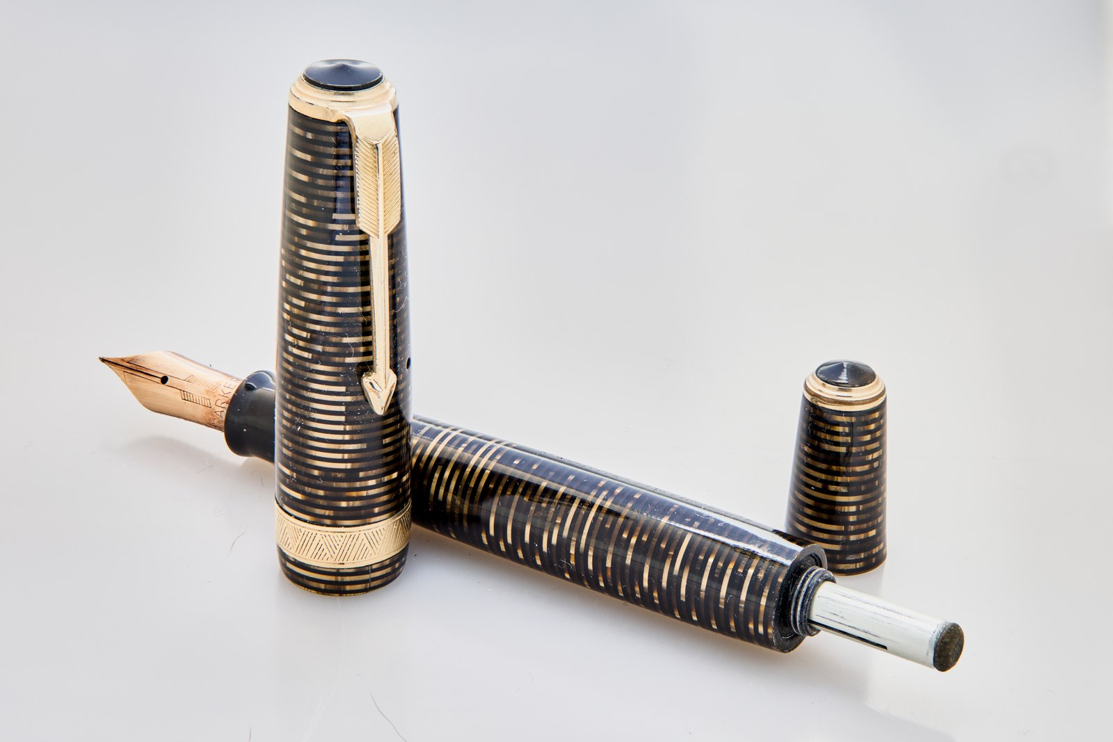 Parker Vacumatic fountain pen with a gold and black striped barrel, its cap standing beside it and the white filler rod extended